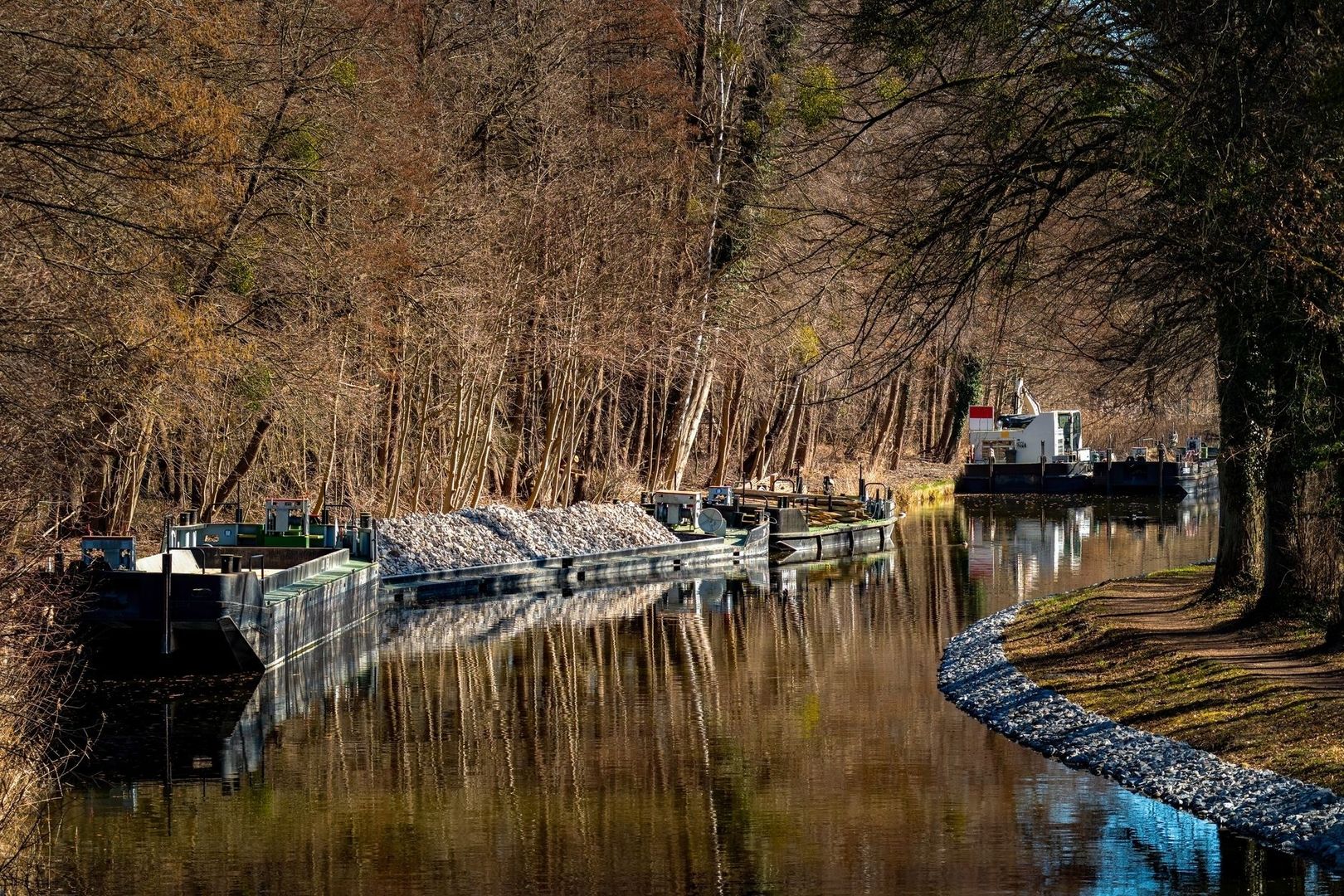 Binnenvaartschepen met steengruis op een rustig, bebost kanaal