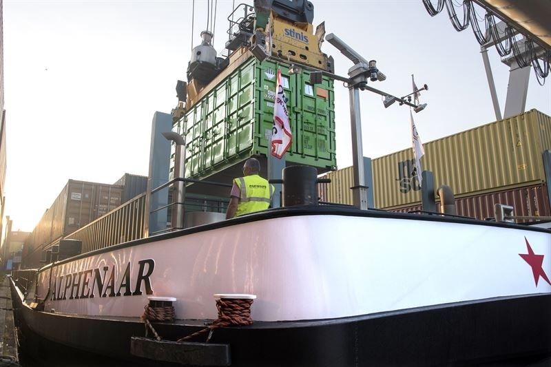 Binnenvaartschip Alphenaer laadt een grote groene container in de haven